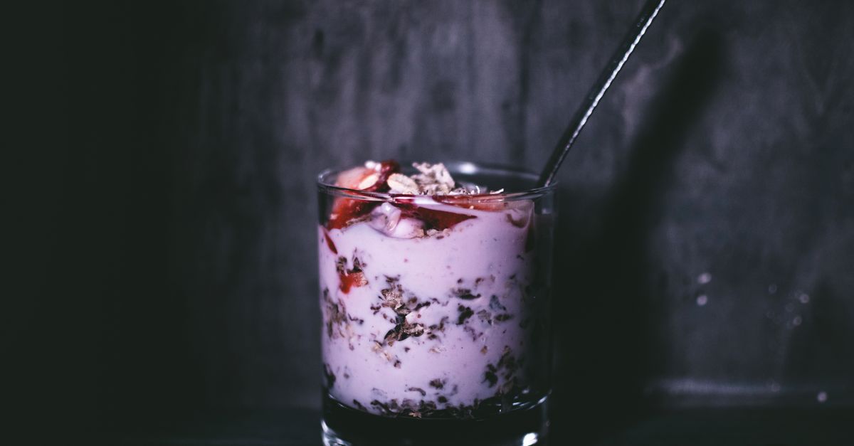 Dark, moody close-up of a delicious yogurt parfait with granola and berries in a glass.